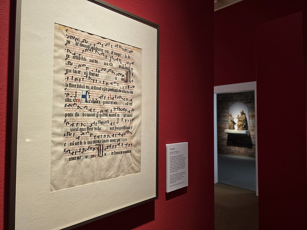 Gerahmtes Notenblatt mit Neumen an einer roten Ausstellungswand