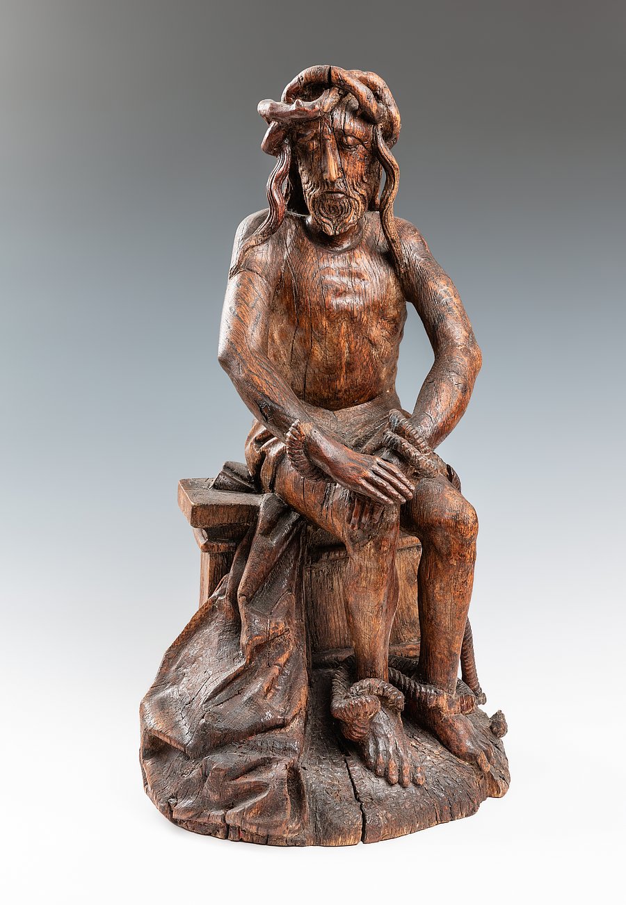 Holzskulptur: Christus sitzt mit gefesselten Händen auf einem Stein, den Kopf in die Hand gestützt