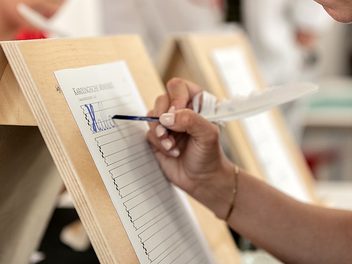 Eine Hand trägt sich in eine Liste auf einem Holzpult ein