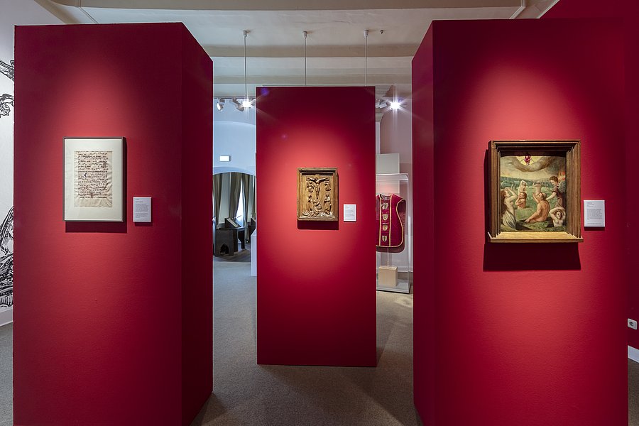 Ausstellungsraum mit roten Stellwänden und gerahmten Werken