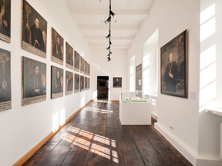 Langer heller Saal mit einer Reihe gerahmter Abtporträts an der Wand
