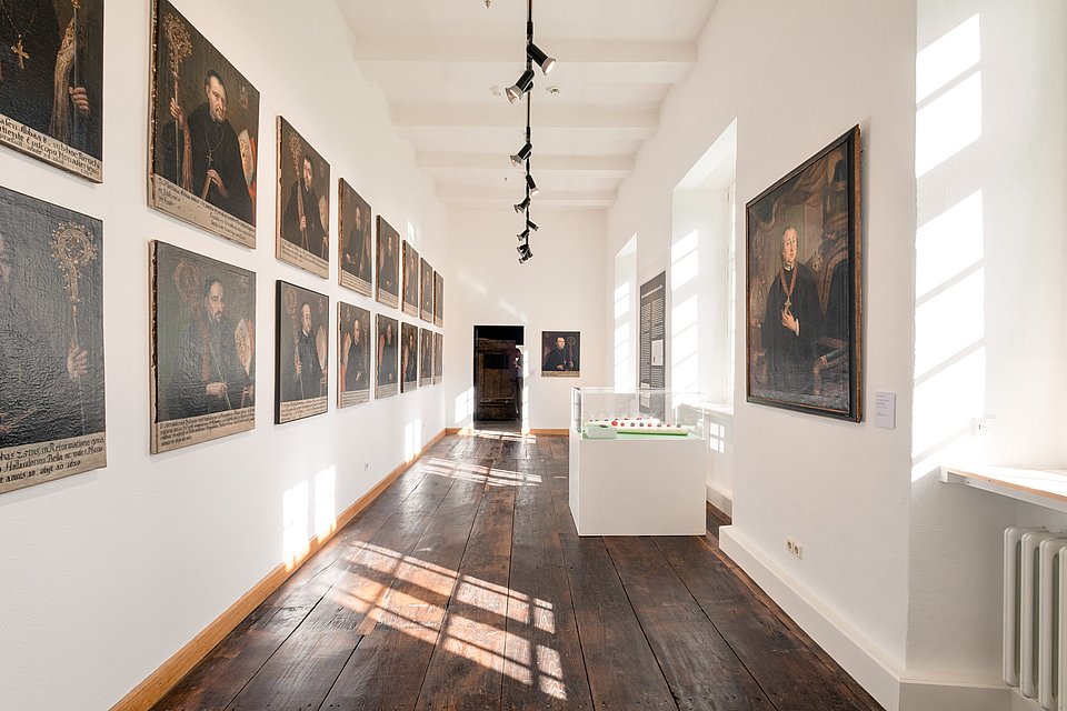 Langer heller Saal mit einer Reihe gerahmter Abtporträts an der Wand