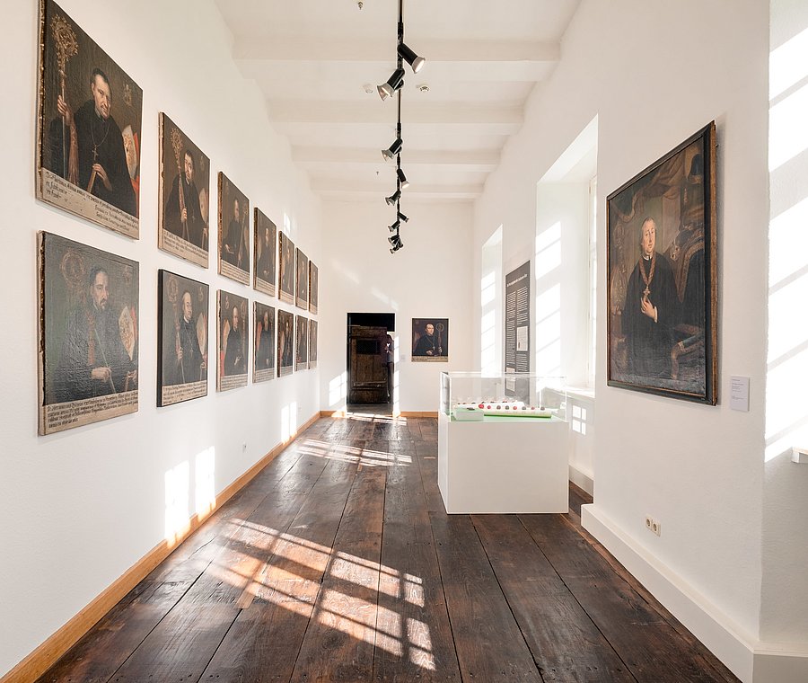 Langer heller Saal mit einer Reihe gerahmter Abtporträts an der Wand