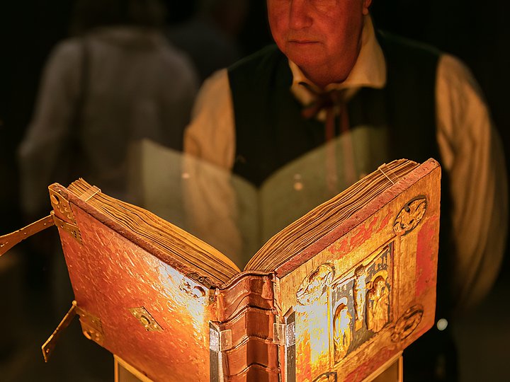 Ein Besucher betrachtet ein aufgeschlagenes, golden leuchtendes Buch in der Vitrine