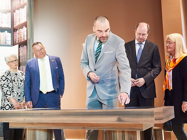 Eine Gruppe steht um einen Tisch vor einer Wand mit Bücherregal-Motiv