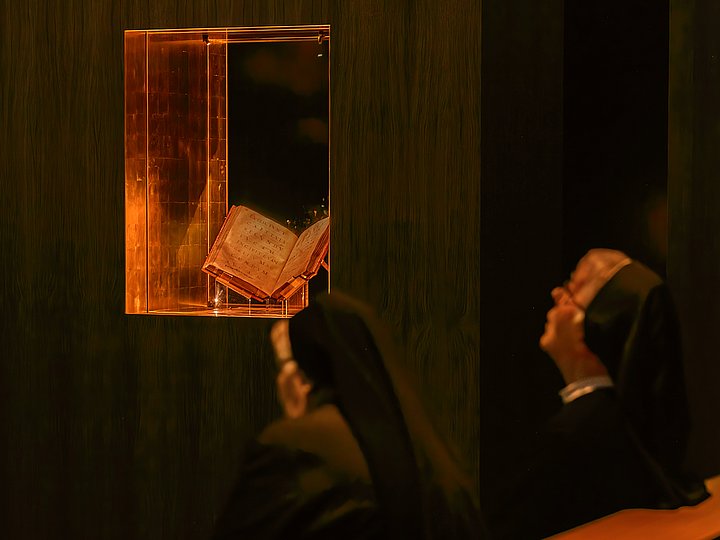 Zwei Ordensschwestern betrachten das beleuchtete Evangeliar in der Vitrine