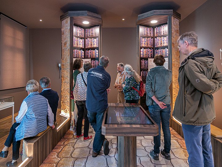 Besucher an einem beleuchteten Medientisch vor Regalen mit Buchrücken