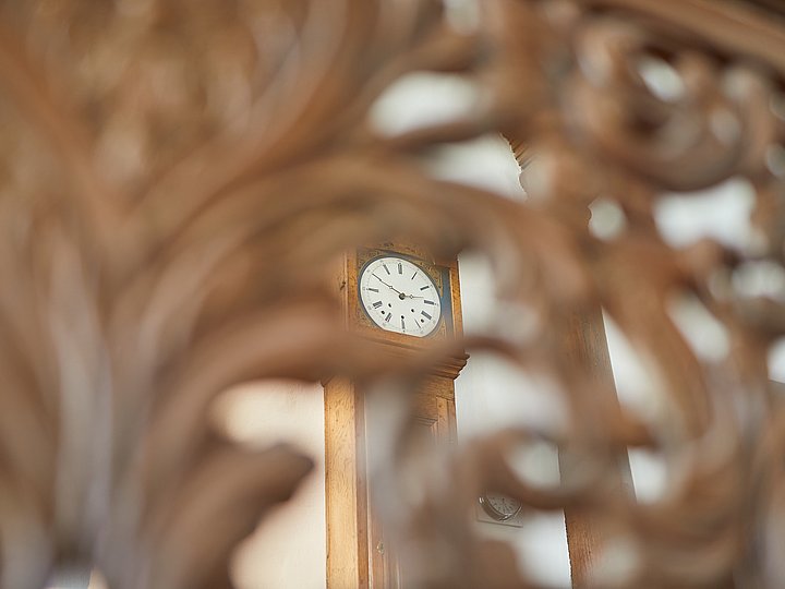 Geschnitztes Ornament, dahinter unscharf eine Uhr