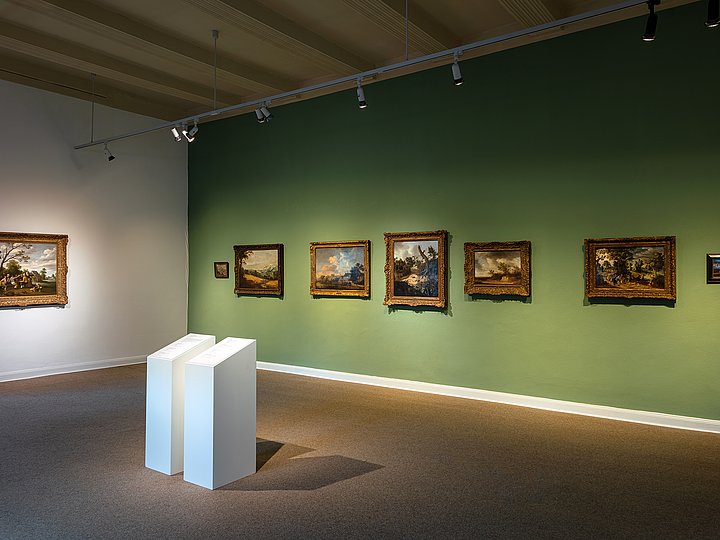 Grün gestrichene Wand mit gerahmten Gemälden, davor weiße Stelen