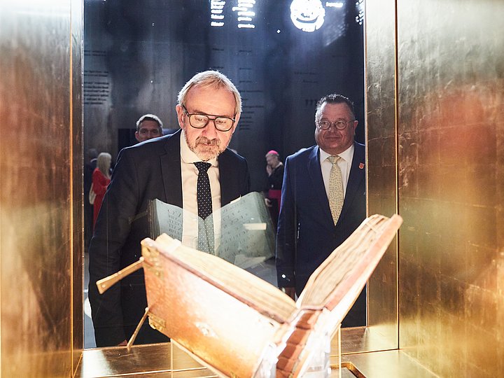 Zwei Gäste betrachten das aufgeschlagene Evangeliar in seiner Vitrine