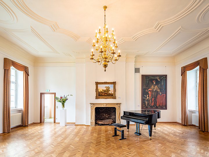 Festsaal mit Kronleuchter, Kamin und Flügel