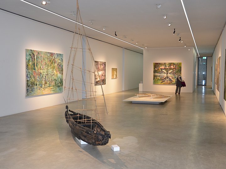 Ausstellungssaal mit Gemälden an den Wänden und einem Boot als Objekt