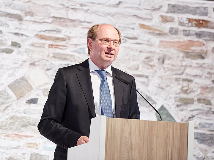 Ein Redner am Pult vor der Bruchsteinwand des Museums