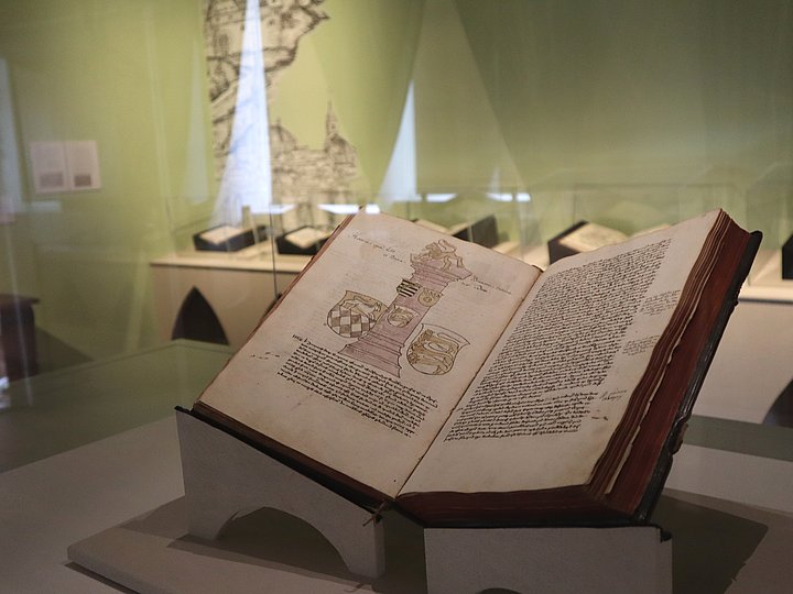 Vitrine mit einem aufgeschlagenen Buch, dahinter ein grüner Vorhang
