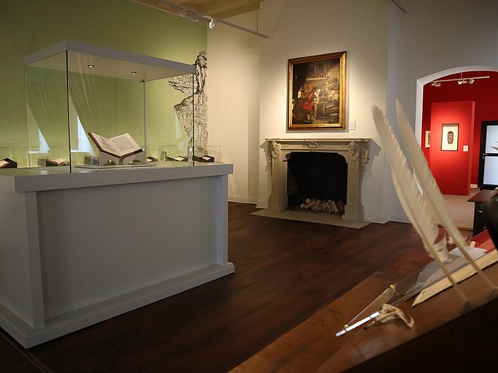 Ausstellungsraum mit Vitrine, Kamin und einem Gemälde darüber