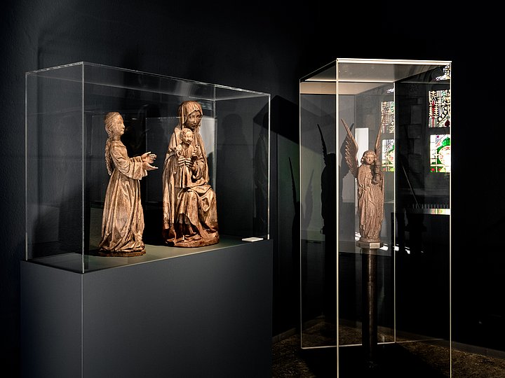 Vitrine mit Holzfiguren in einem abgedunkelten Raum