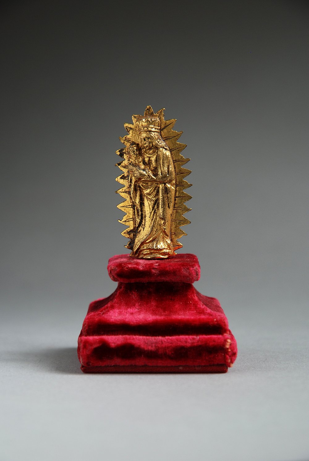 Vergoldete Madonnenfigur in einer Flammengloriole auf einem roten Samtsockel